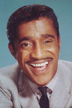 Portrait of Sammy Davis Jr., a legendary Jewish American entertainer and member of the Rat Pack. He is captured with a bright, infectious smile, wearing a light gray suit and a black tie. His charismatic and joyful expression reflects his versatile talents that spanned across singing, dancing, and acting, making him a beloved figure in American entertainment history.